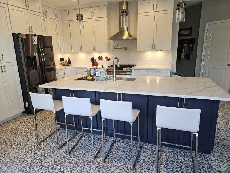 Modern kitchen with navy island, marble countertop, white cabinets, patterned tile floor, and stainless steel appliances.